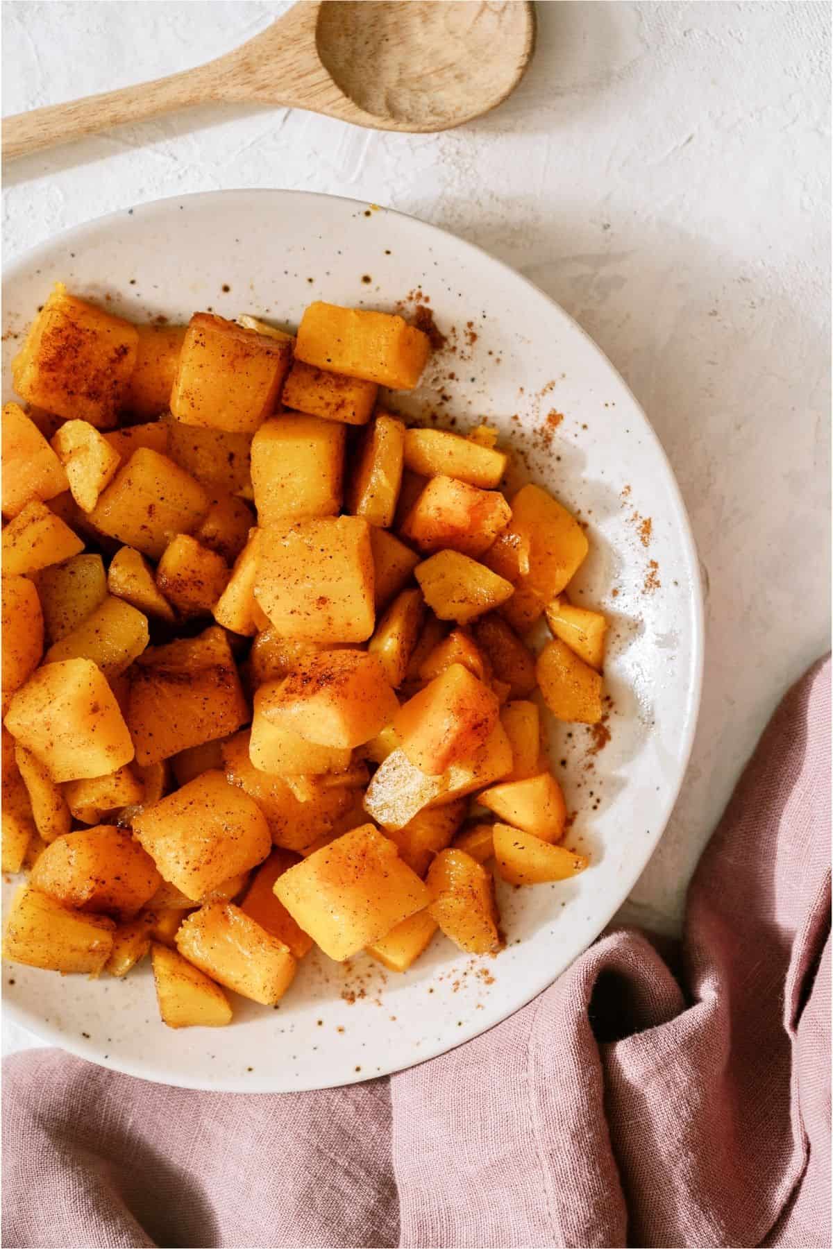 Top view of Maple Roasted Butternut Squash in a white bowl with a wooden spoon on the side.