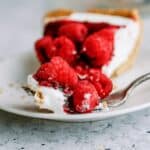 A slice of Raspberry Cream Cheese Pie topped with fresh raspberries on a plate with a fork.