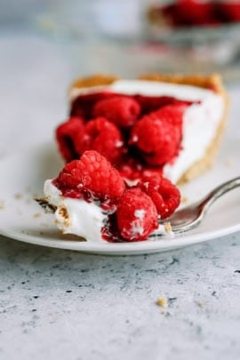 A slice of Raspberry Cream Cheese Pie topped with fresh raspberries on a plate with a fork.