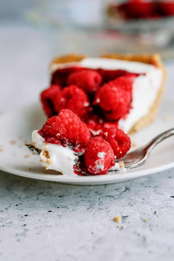 A slice of Raspberry Cream Cheese Pie topped with fresh raspberries on a plate with a fork.