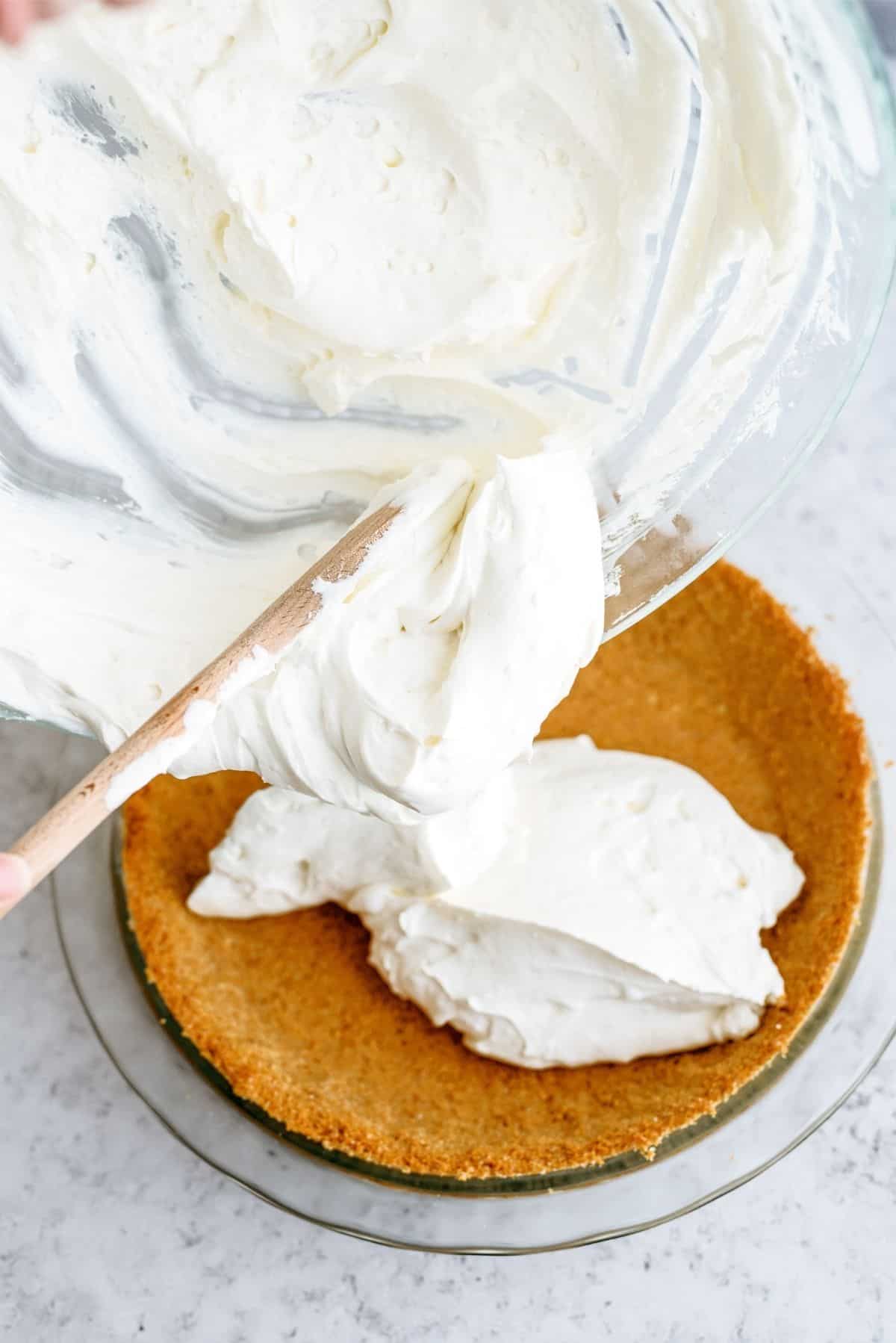 Cream cheese mixture being spread into graham cracker crust