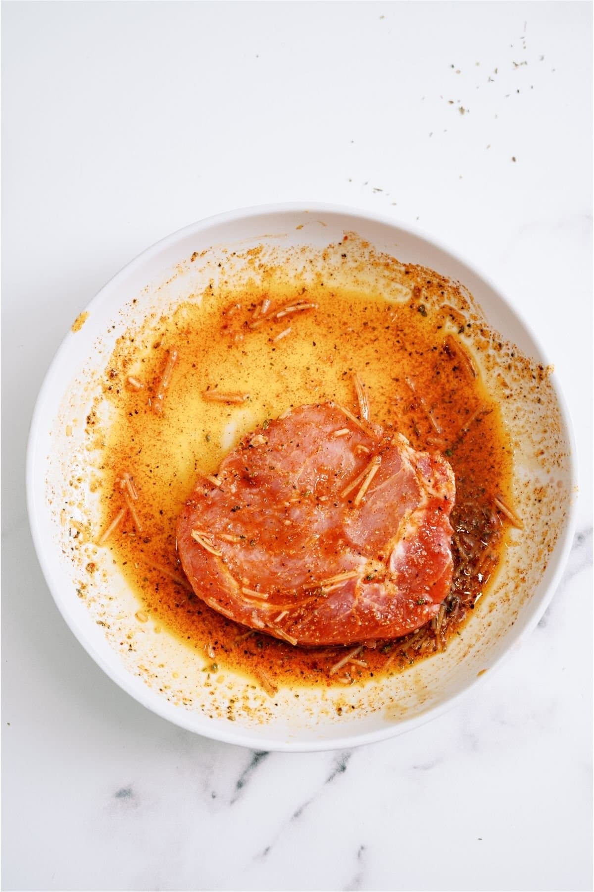 A pork chop with both sides dipped in bowl of Italian dressing mixture.