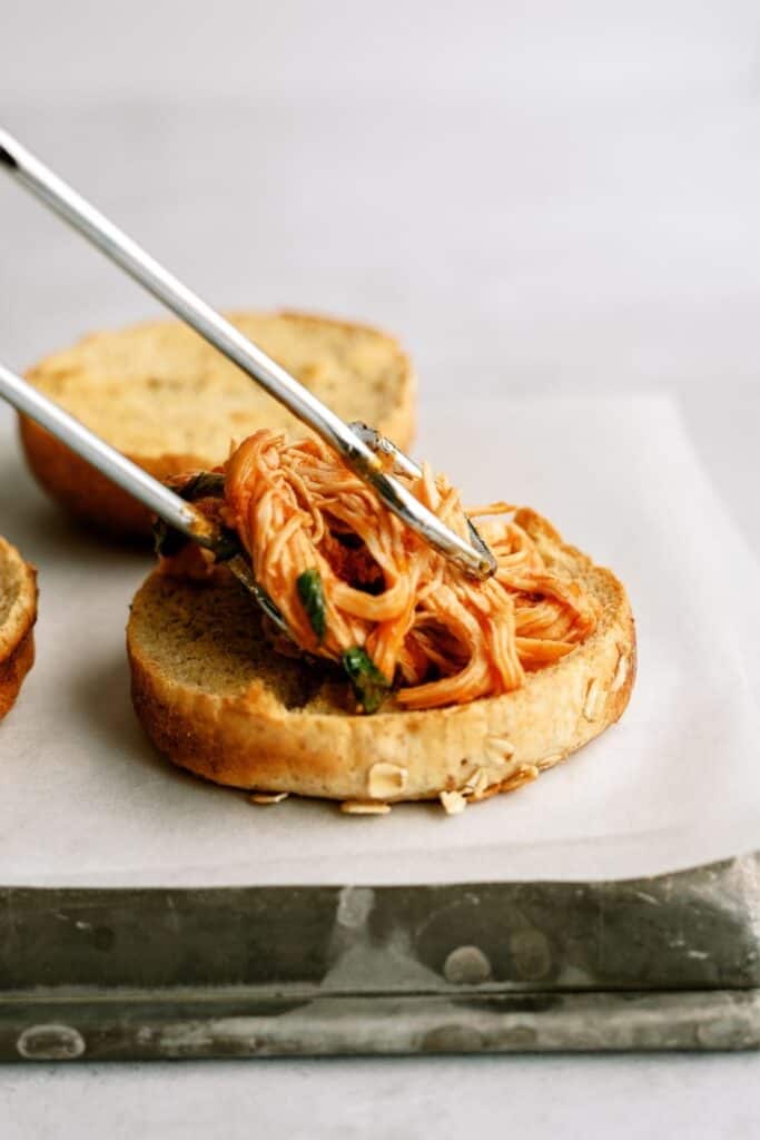 Tongs placing Italian shredded chicken on a bun.