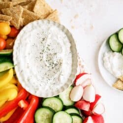 Top view of a bowl of Vegetable Dill Dip on a platter with chopped veggies and crackers.