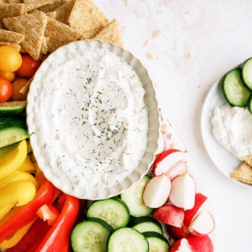 Top view of a bowl of Vegetable Dill Dip on a platter with chopped veggies and crackers.