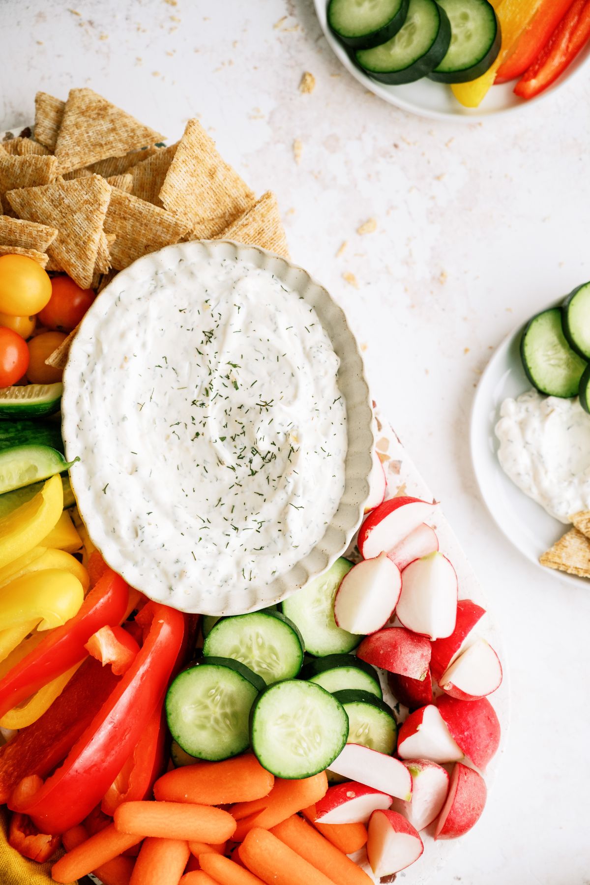 Top view of a bowl of Vegetable Dill Dip on a platter with chopped veggies and crackers.