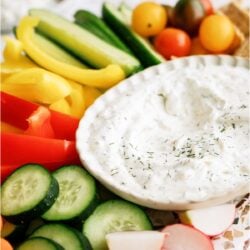A white bowl of Vegetable Dill Dip on a platter with sliced veggies surrounding it.