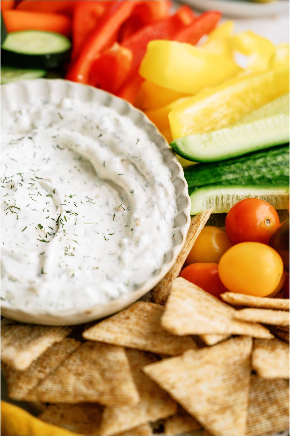 Close up of a bowl of Vegetable Dill Dip on a platter surrounded by sliced veggies and crackers.
