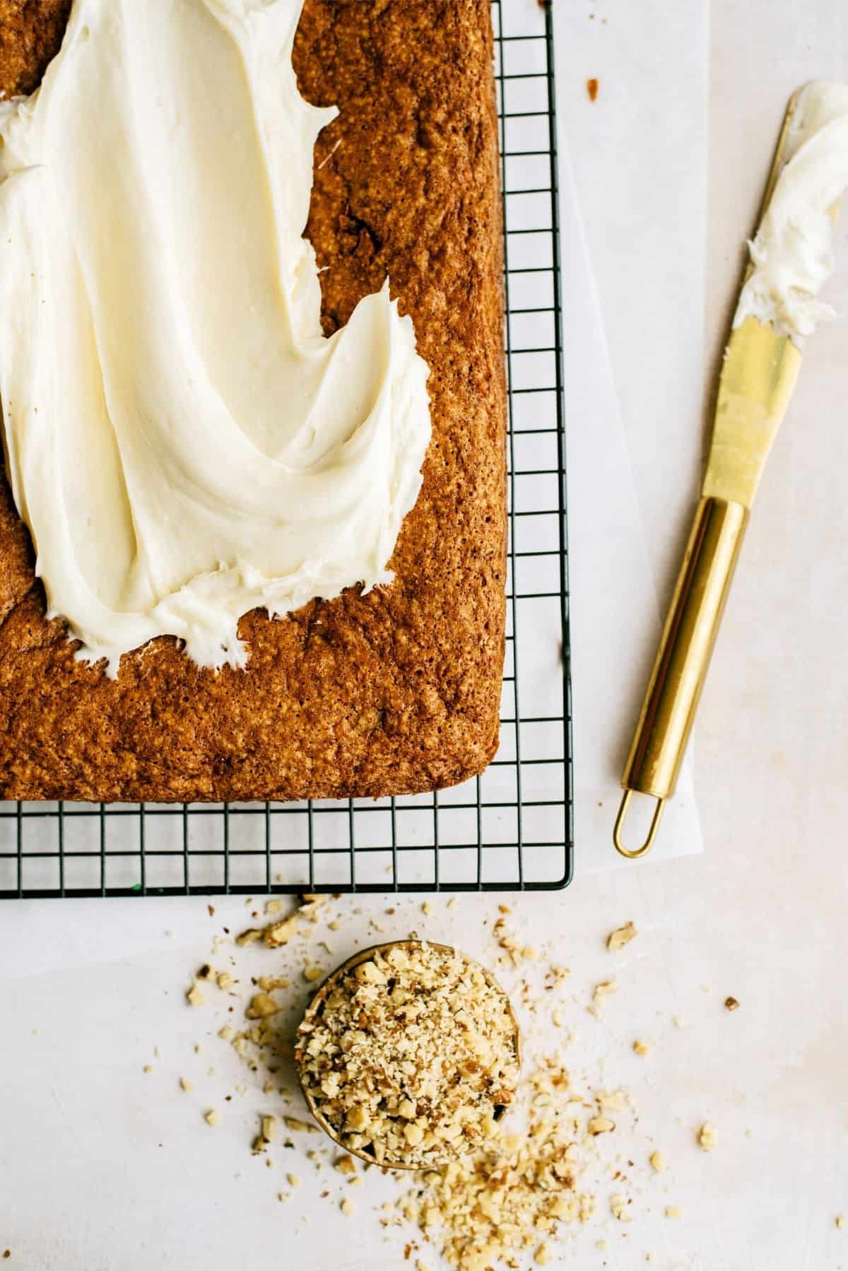 Carrot cake on a cooling rack with half of it frosted