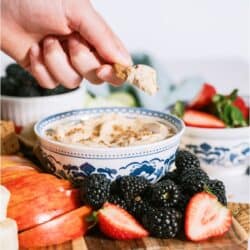 Brown Sugar Cream Cheese Fruit Dip in a bowl surrounded by fruit with one piece being dipped in bowl.