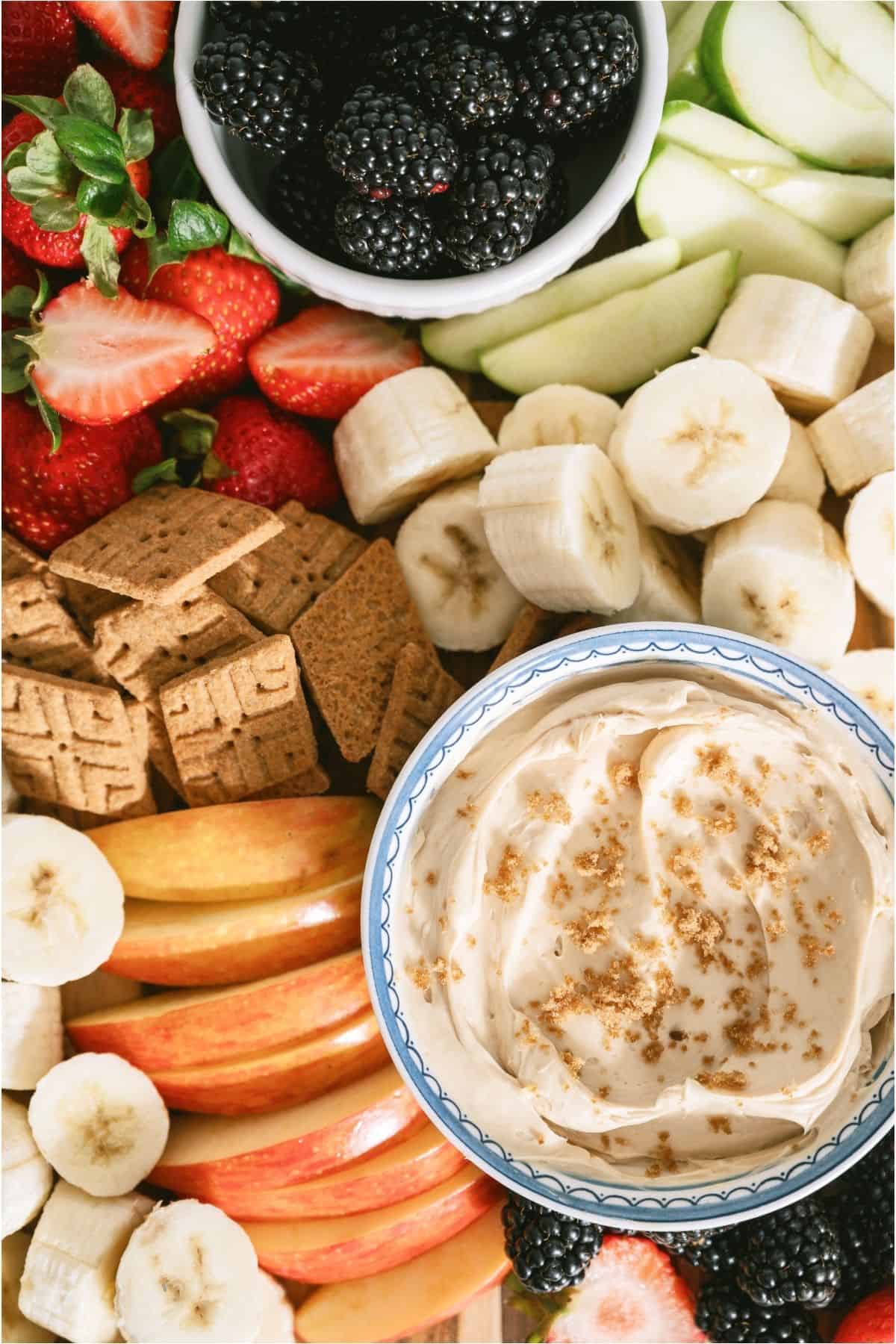 A bowl of Brown Sugar Cream Cheese Fruit Dip on a board of different sliced fruits and crackers.