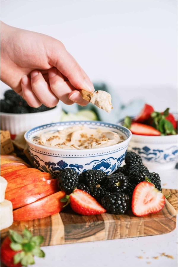 Brown Sugar Cream Cheese Fruit Dip in a bowl surrounded by fruit with one piece being dipped in bowl.