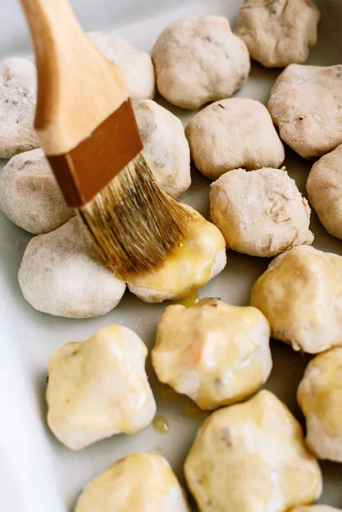 Brushing the tops of the unbaked rolls with butter