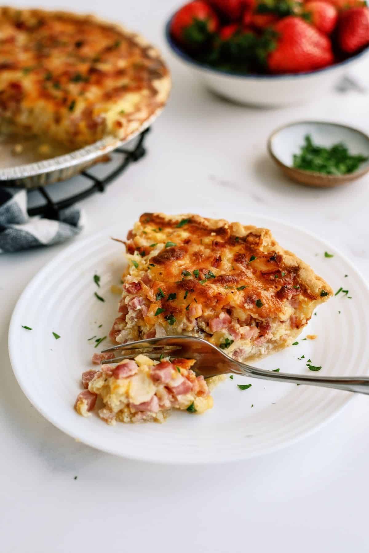 A fork slicing a piece of Easy Ham and Cheese Quiche on a plate