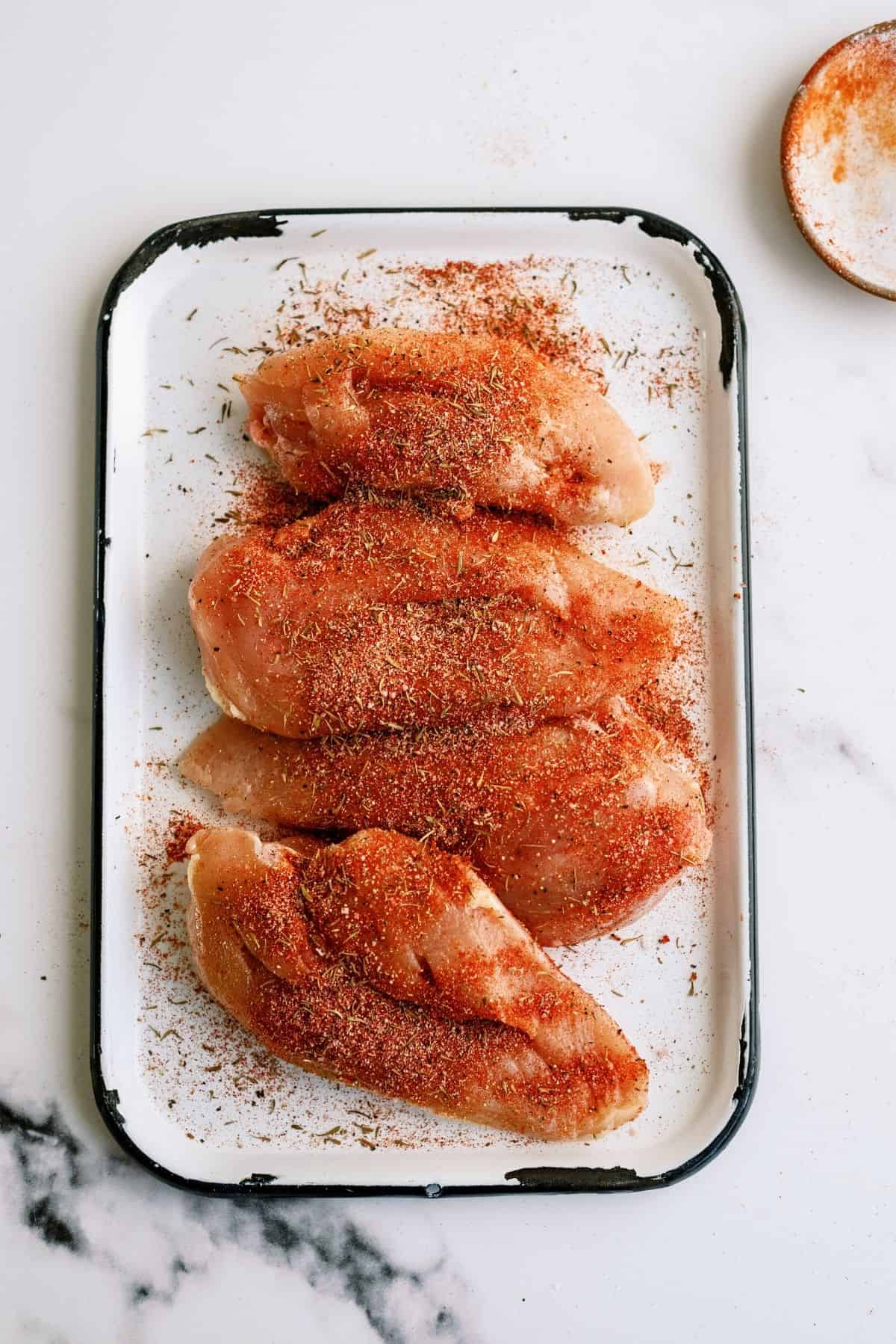 Chicken breast on a cutting board with seasoning sprinkled on top