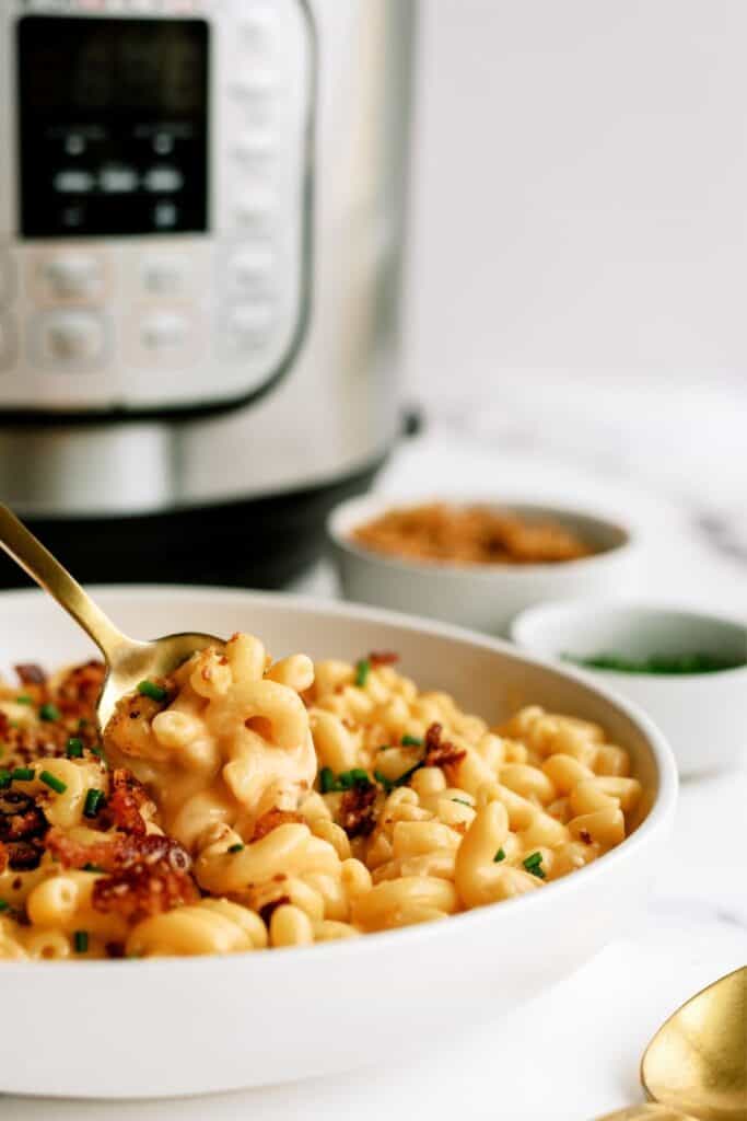 A serving of Instant Pot Loaded Mac and Cheese in a white bowl with the Instant Pot in the background.