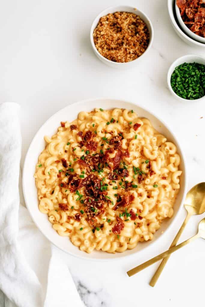 A bowl of Instant Pot Loaded Mac and Cheese with more toppings on the side.