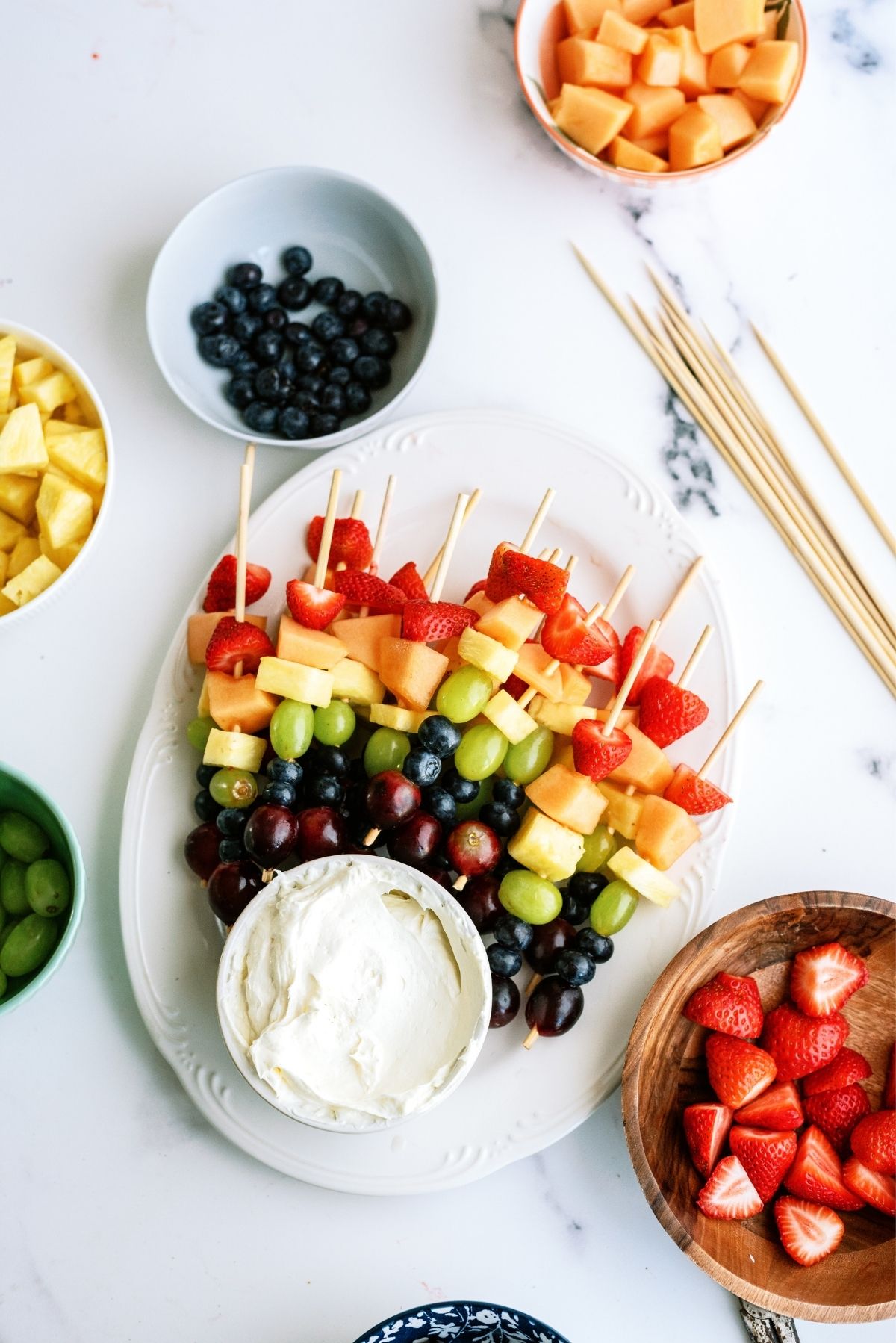 Rainbow Fruit Kabobs with Fluffy Marshmallow Dip surrounded by bowls of fruit