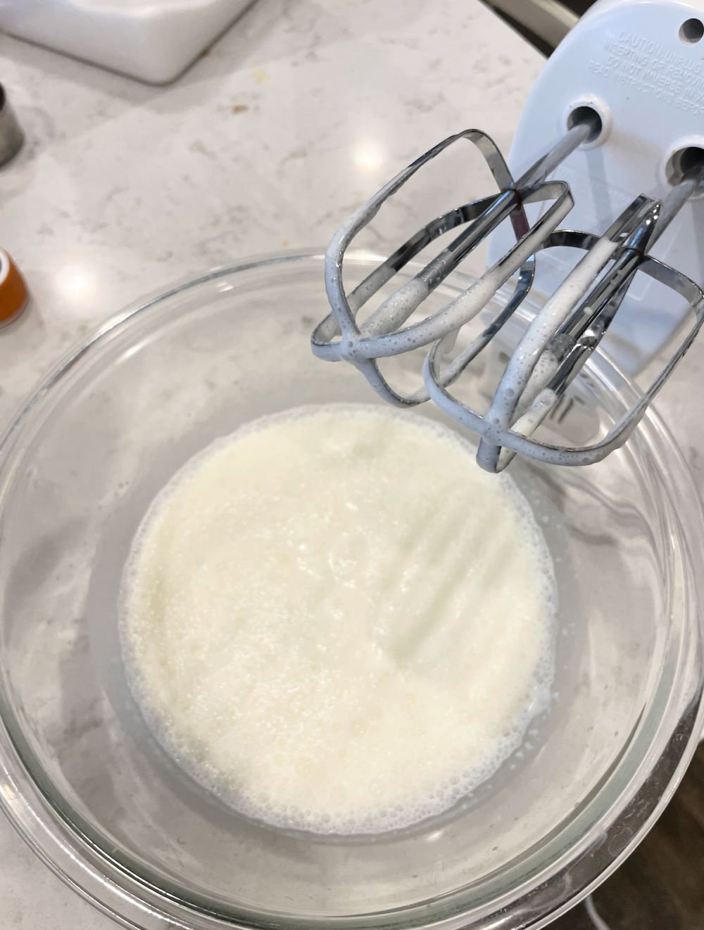 Whipped cream in a mixing bowl with hand mixer