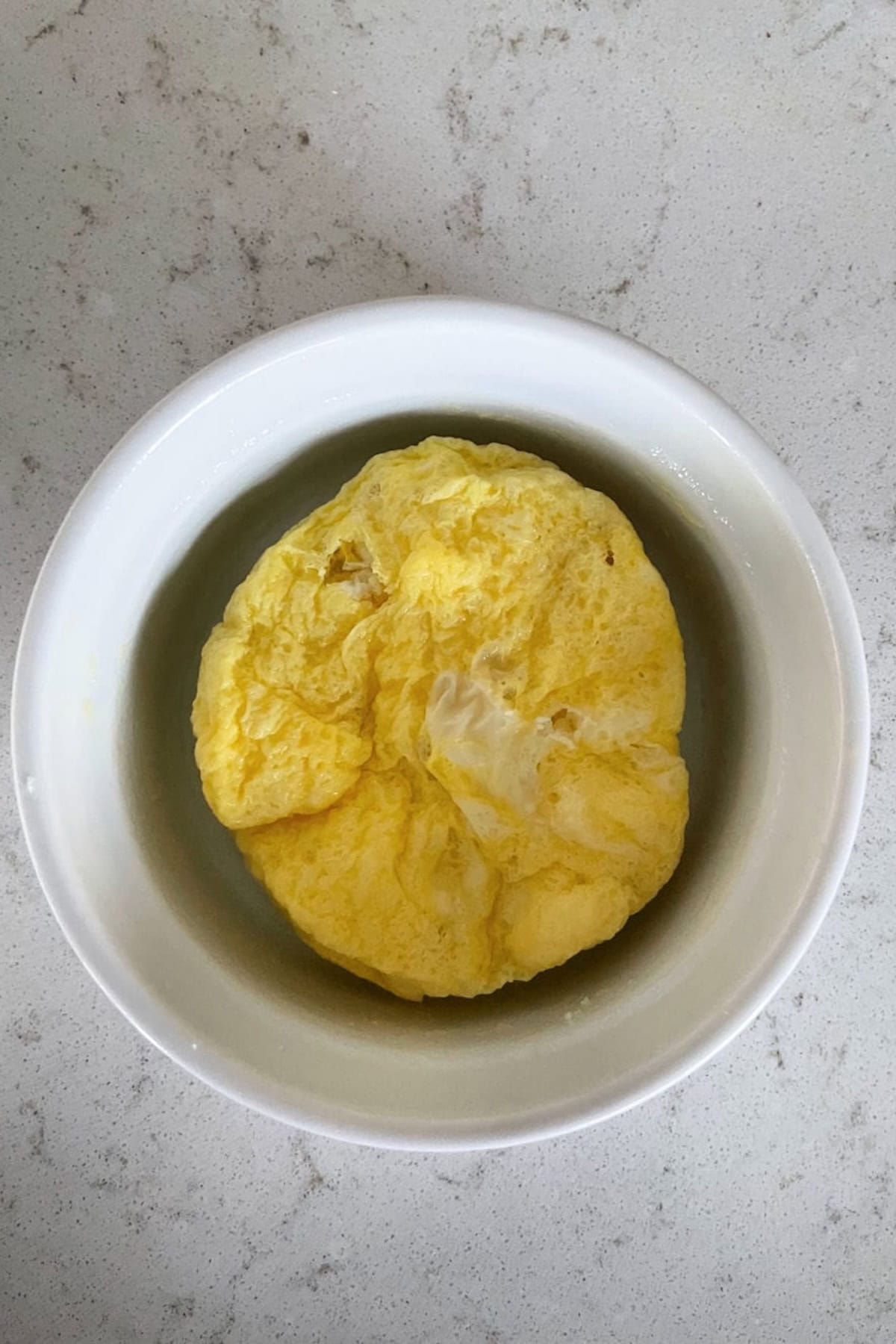 A fluffy yellow egg omelette in a white bowl on a light-colored countertop.