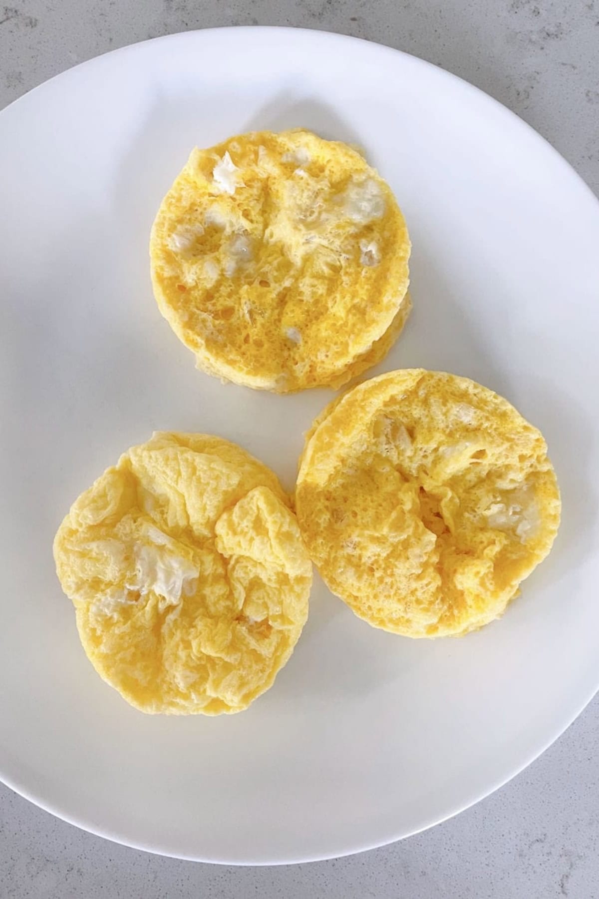 Three round, fluffy scrambled egg patties on a white plate.