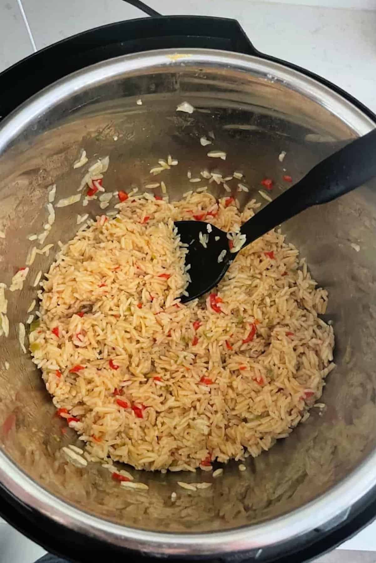 Cooked rice mixed with diced red and green peppers inside a metal pot with a black serving spoon.
