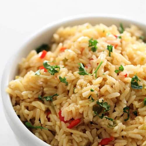 A white bowl filled with cooked rice mixed with chopped red bell peppers and garnished with fresh green herbs.