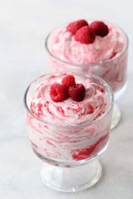 Two glass dessert cups filled with swirled raspberry mousse, each topped with three fresh raspberries.