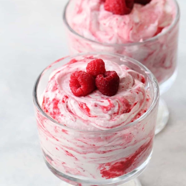 Two glass dessert cups filled with swirled raspberry mousse, each topped with three fresh raspberries.