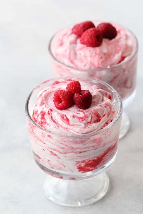 Two glass dessert cups filled with swirled raspberry mousse, each topped with three fresh raspberries.
