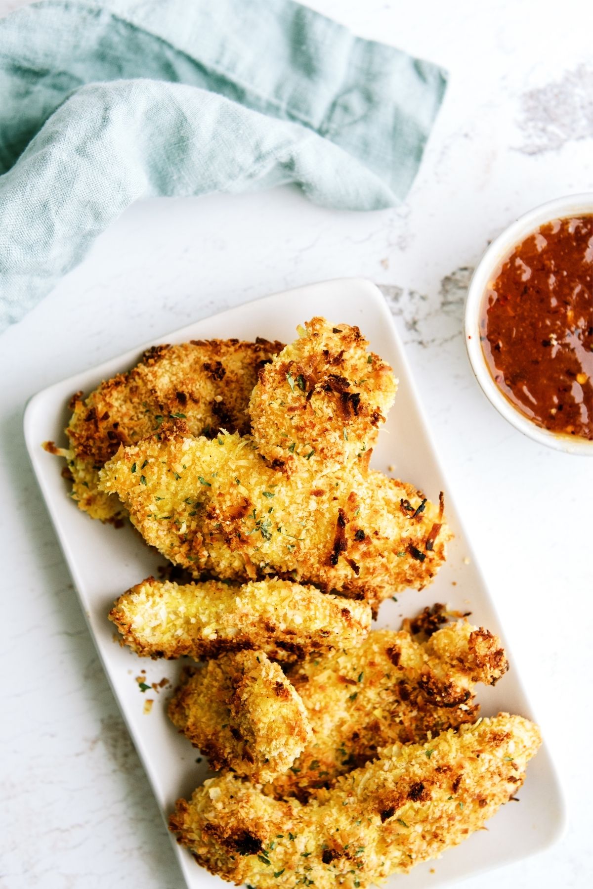 Baked Crispy Coconut Chicken Tenders on a serving plate with a side of sauce