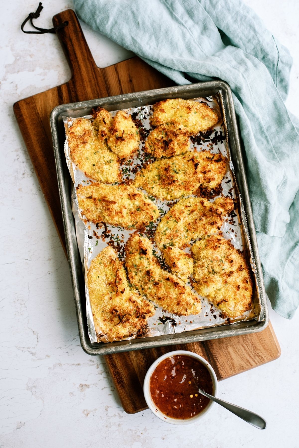 Baked Crispy Coconut Chicken Tenders on a sheet pan with a side of sauce
