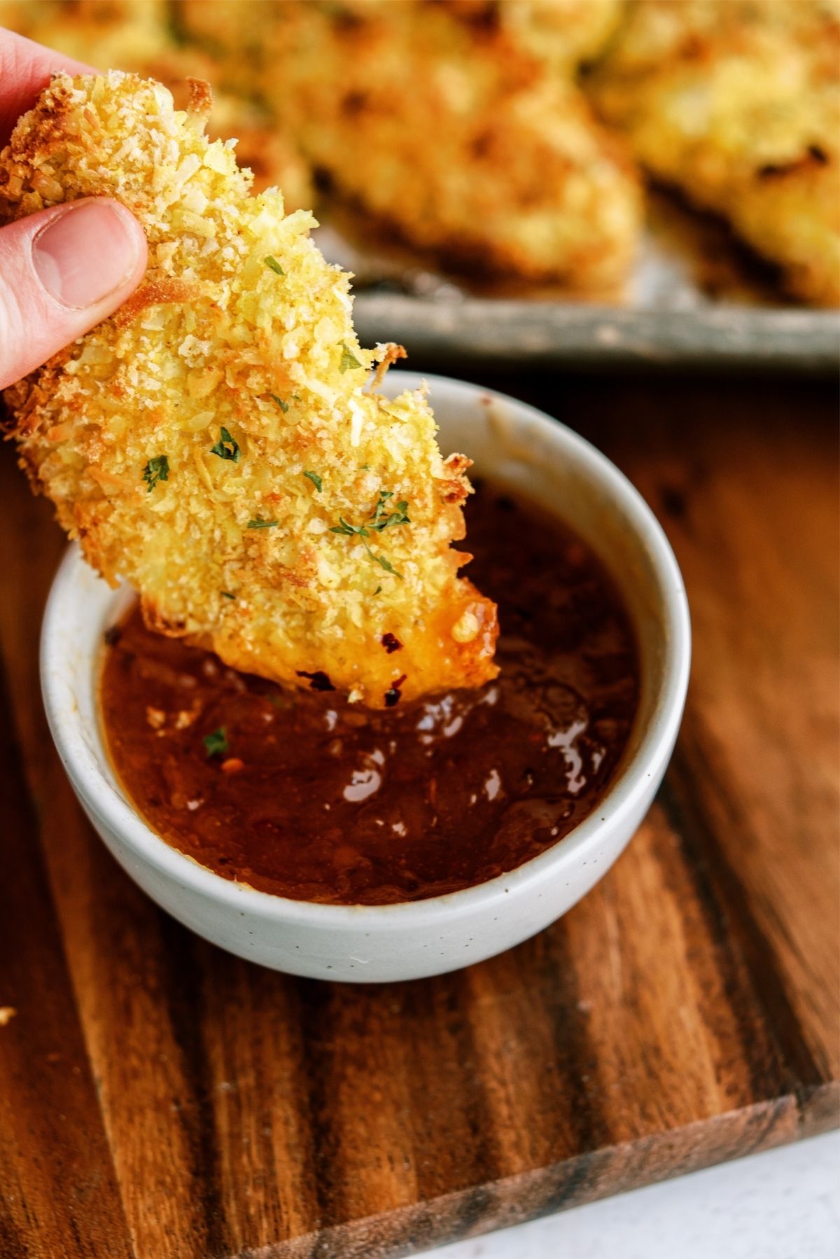 Baked Crispy Coconut Chicken Tender being dipped in sauce