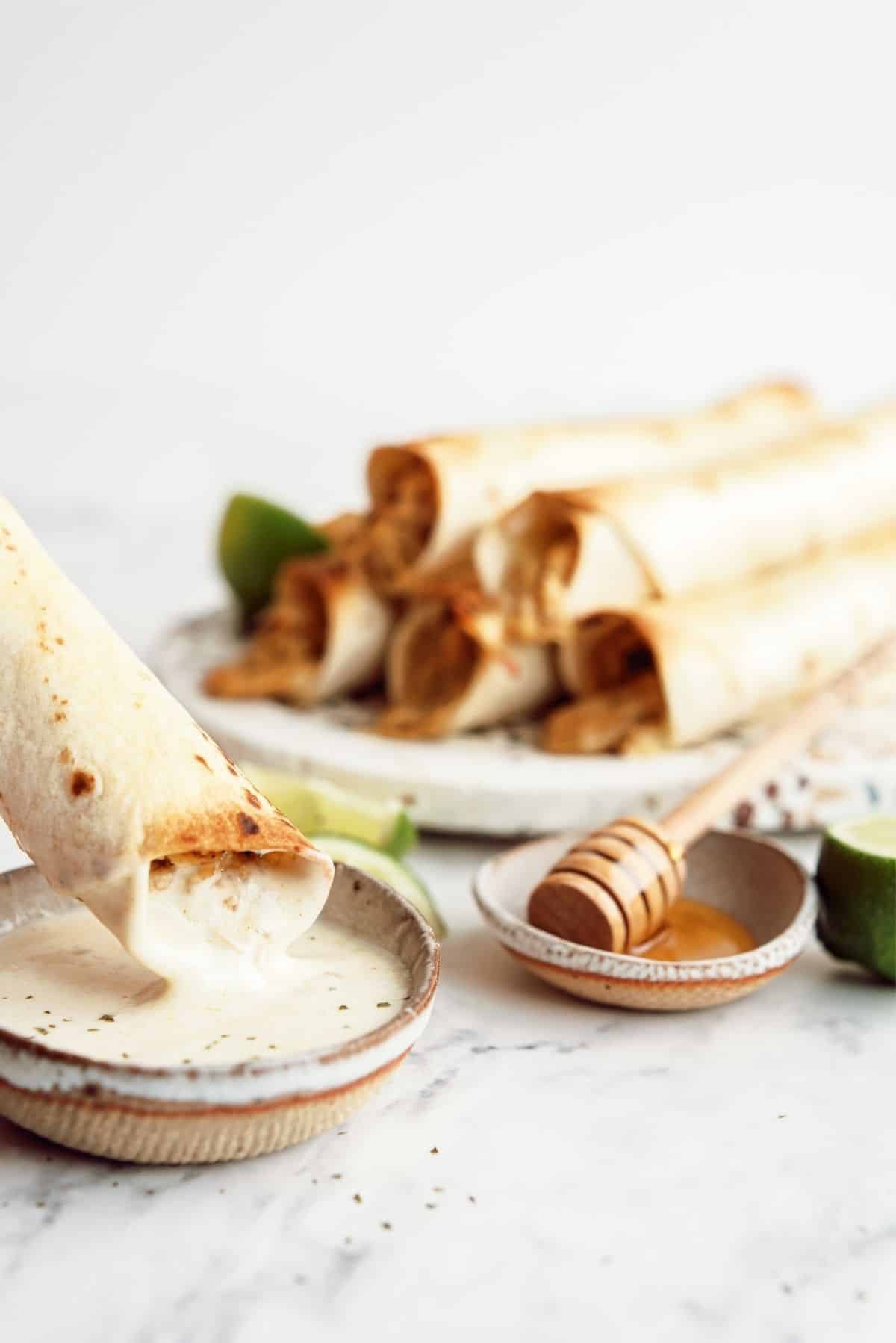 Baked Honey Lime Chicken Taquitos on a plate with one being dipped in ranch