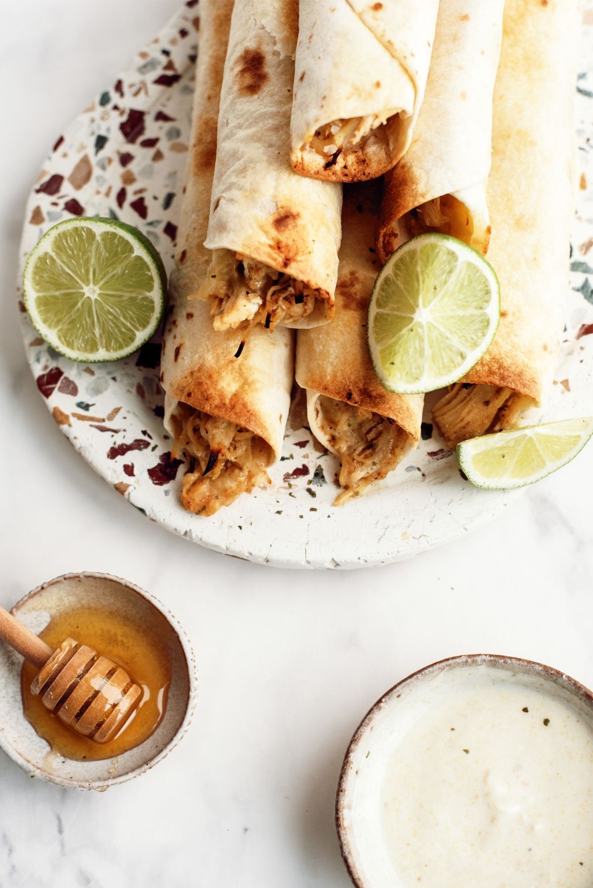 Baked Honey Lime Chicken Taquitos on a plate with a side of ranch and honey