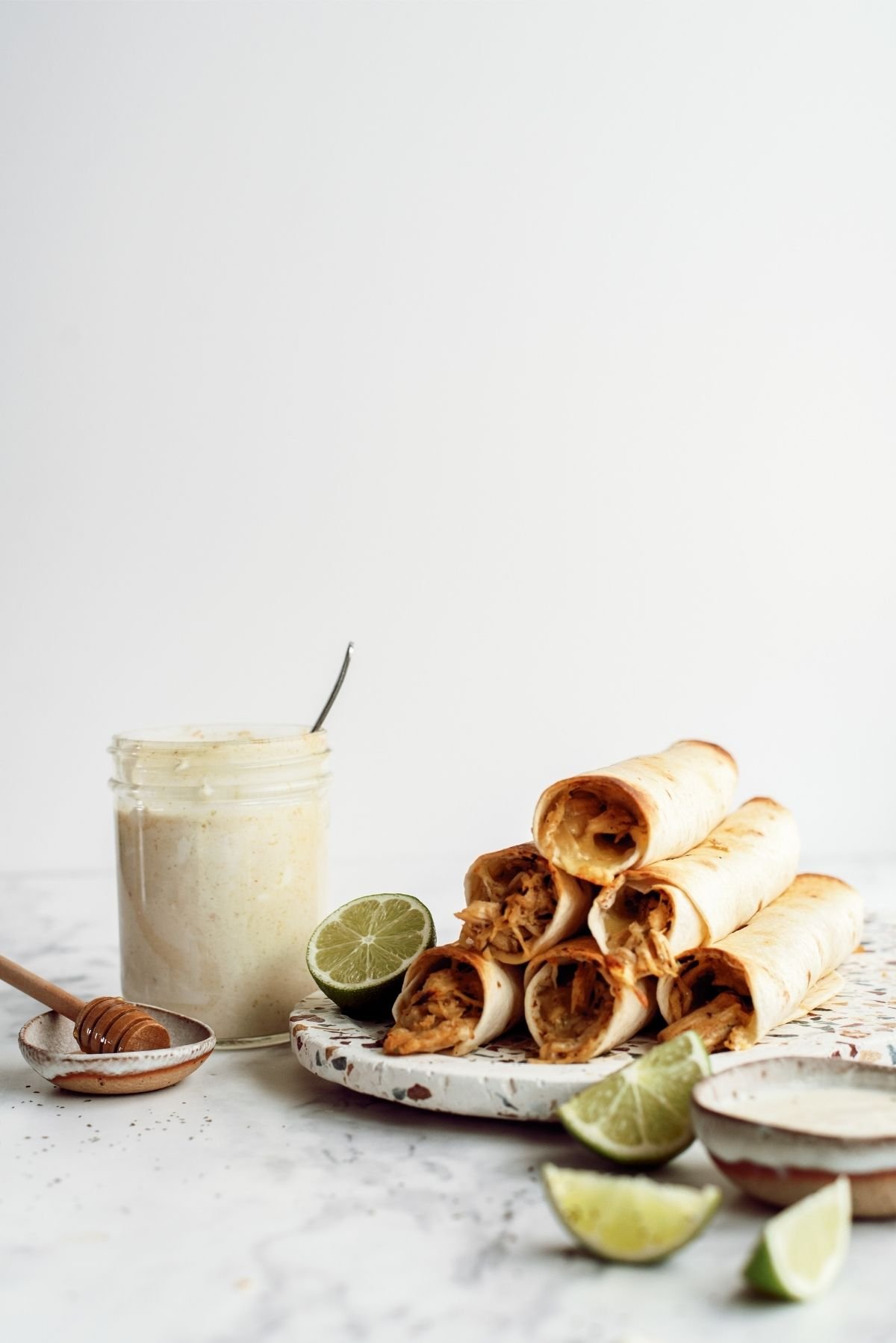 Baked Honey Lime Chicken Taquitos on a plate surrounded with honey, lime and ranch