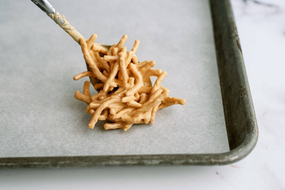 A spoon placing a scoop of chowmein noodles covered in butterscotch mixture on a baking sheet line with wax paper.