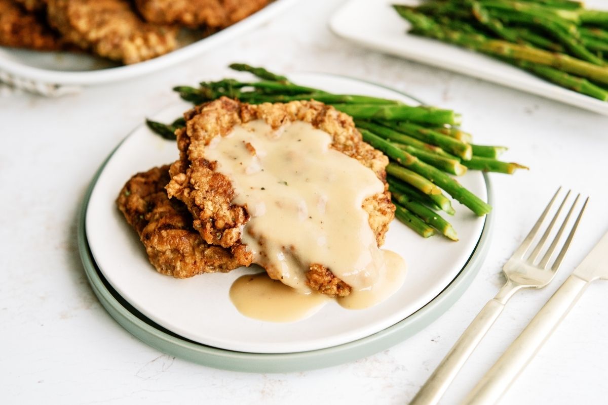 Chicken Fried Steak with Gravy on a plate with asparagus a fork and knife