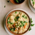A bowl of creamy chicken and vegetable soup garnished with fresh parsley, featuring peas, carrots, potatoes, and chunks of chicken.