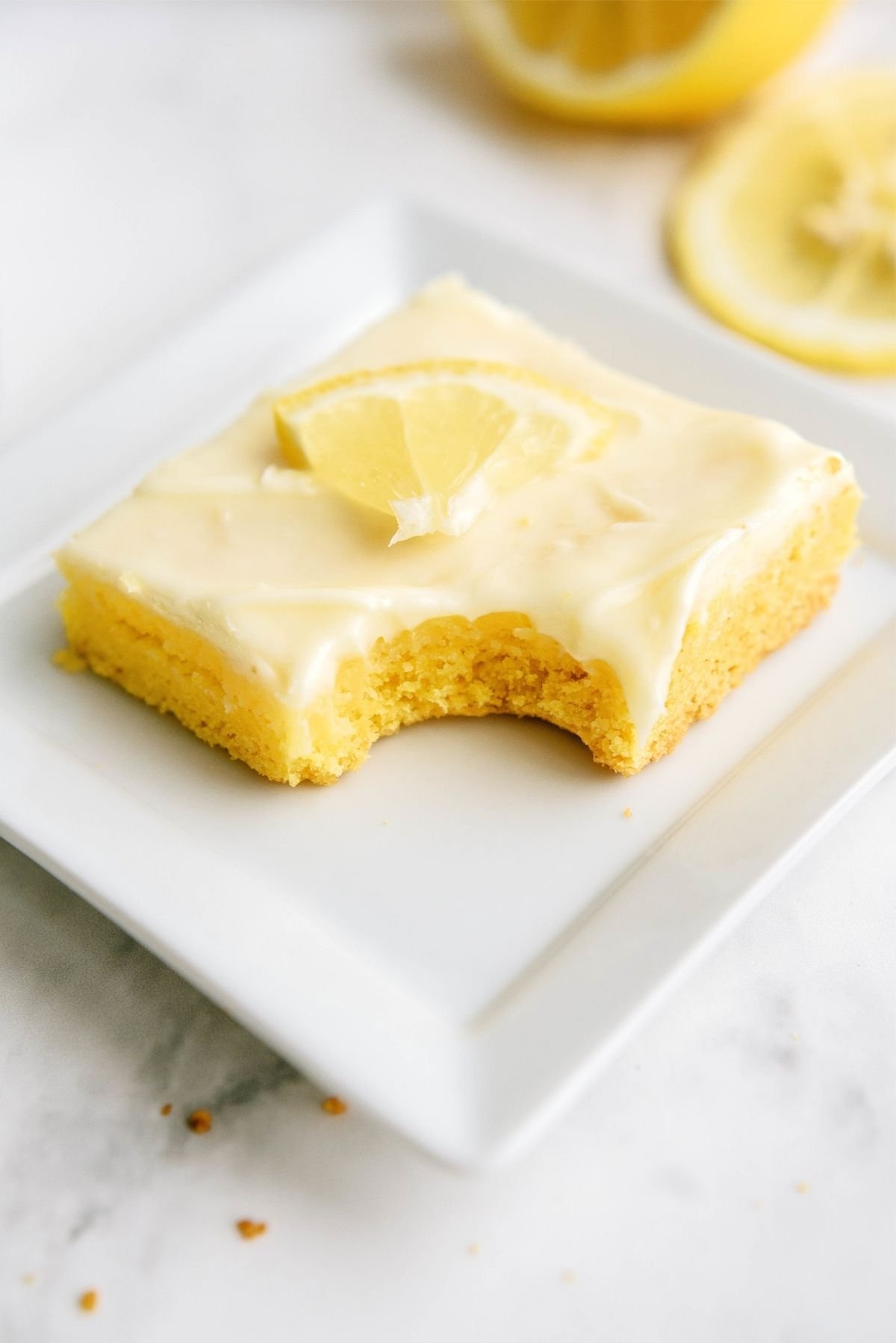 Frosted Gooey Lemon Bar on a plate with a bite missing