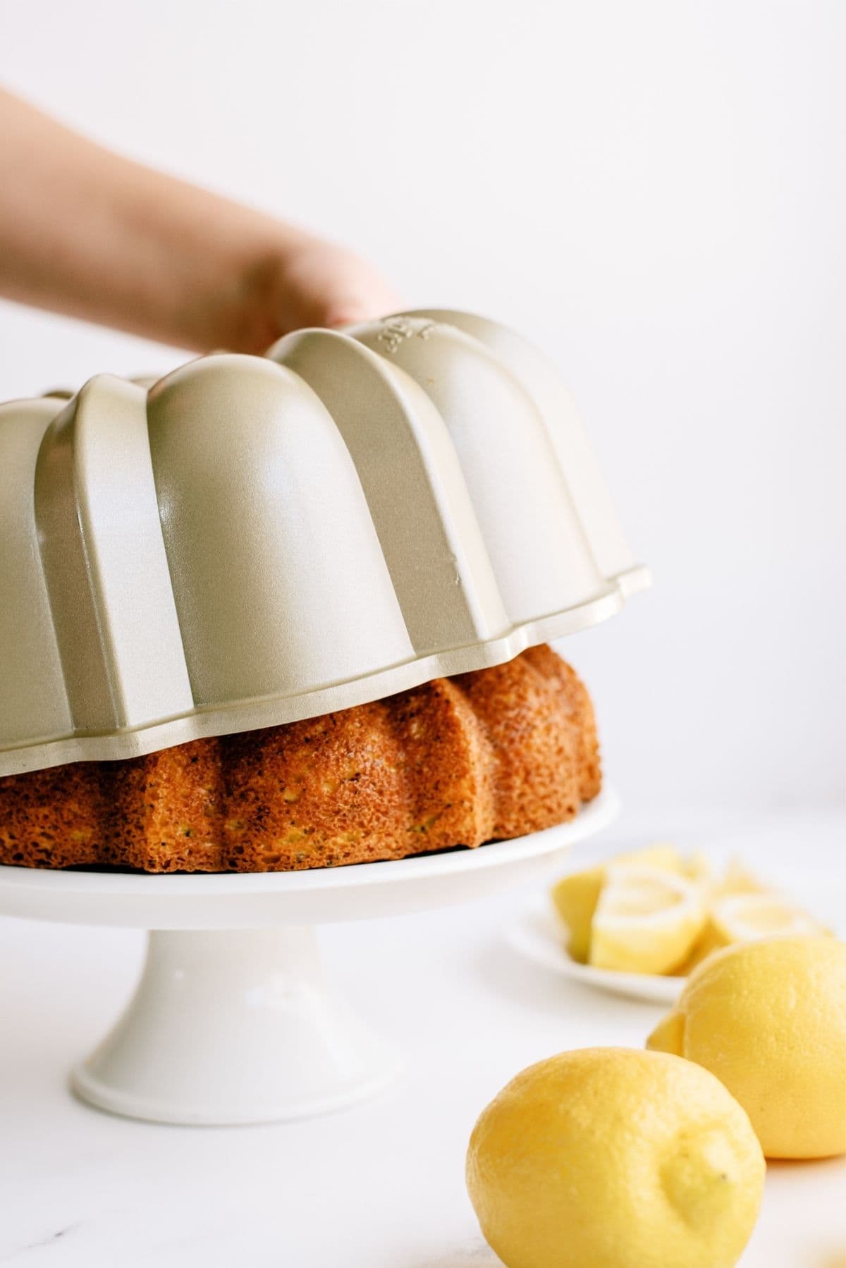 Removing the bundt cake pan from a bundt cake on a cake stand.