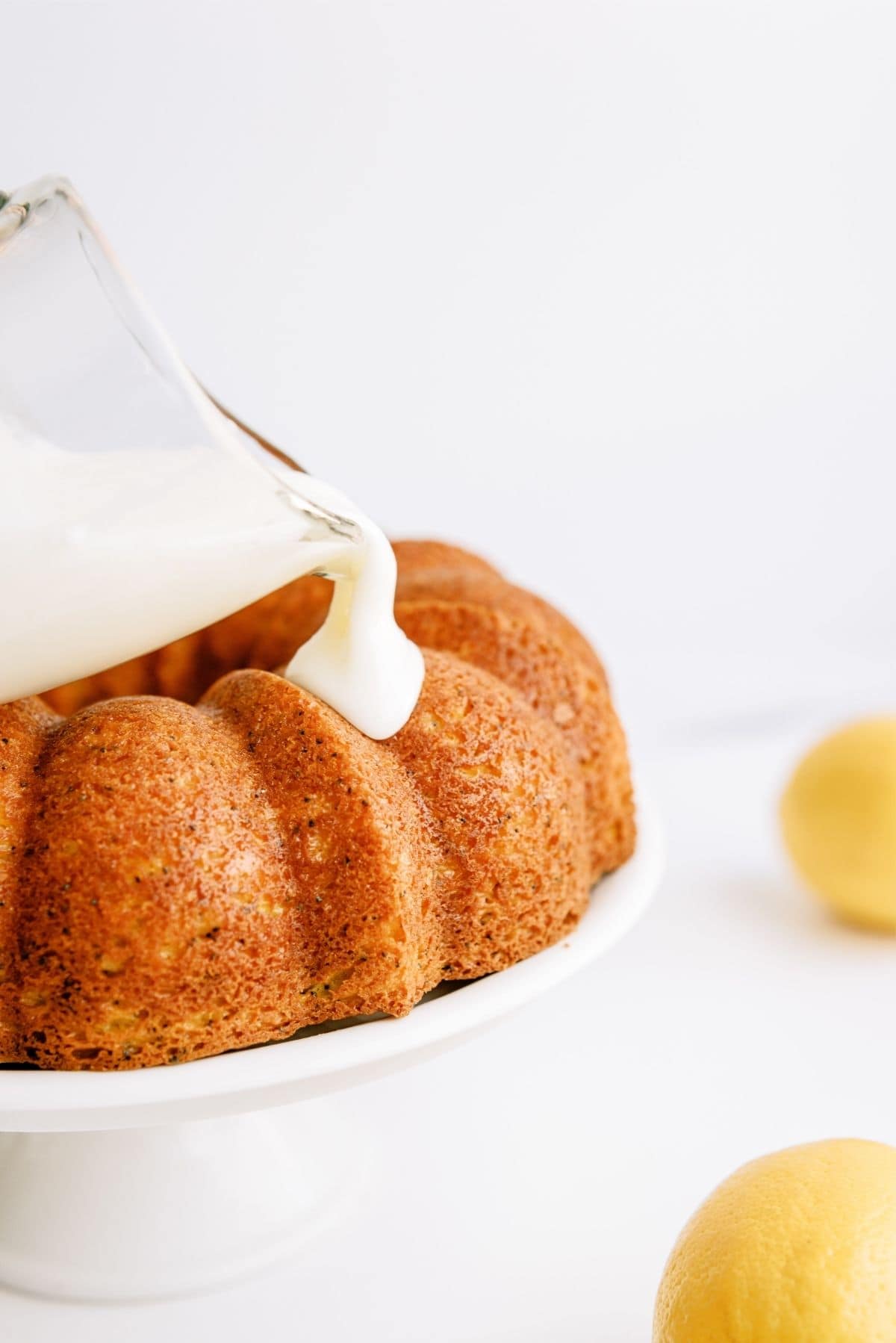 Pouring icing from a glass measuring cup onto a bundt cake on a cake stand.