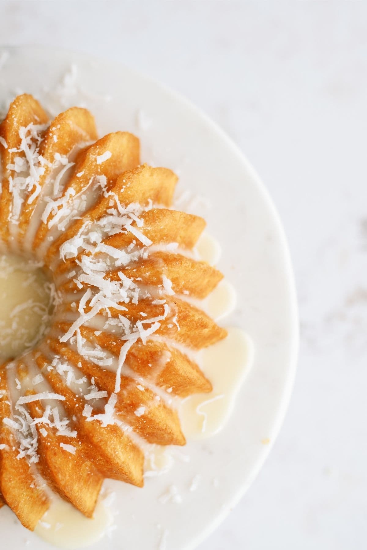 A bundt cake drizzled with icing and sprinkled with shredded coconut on a white plate, viewed from above.