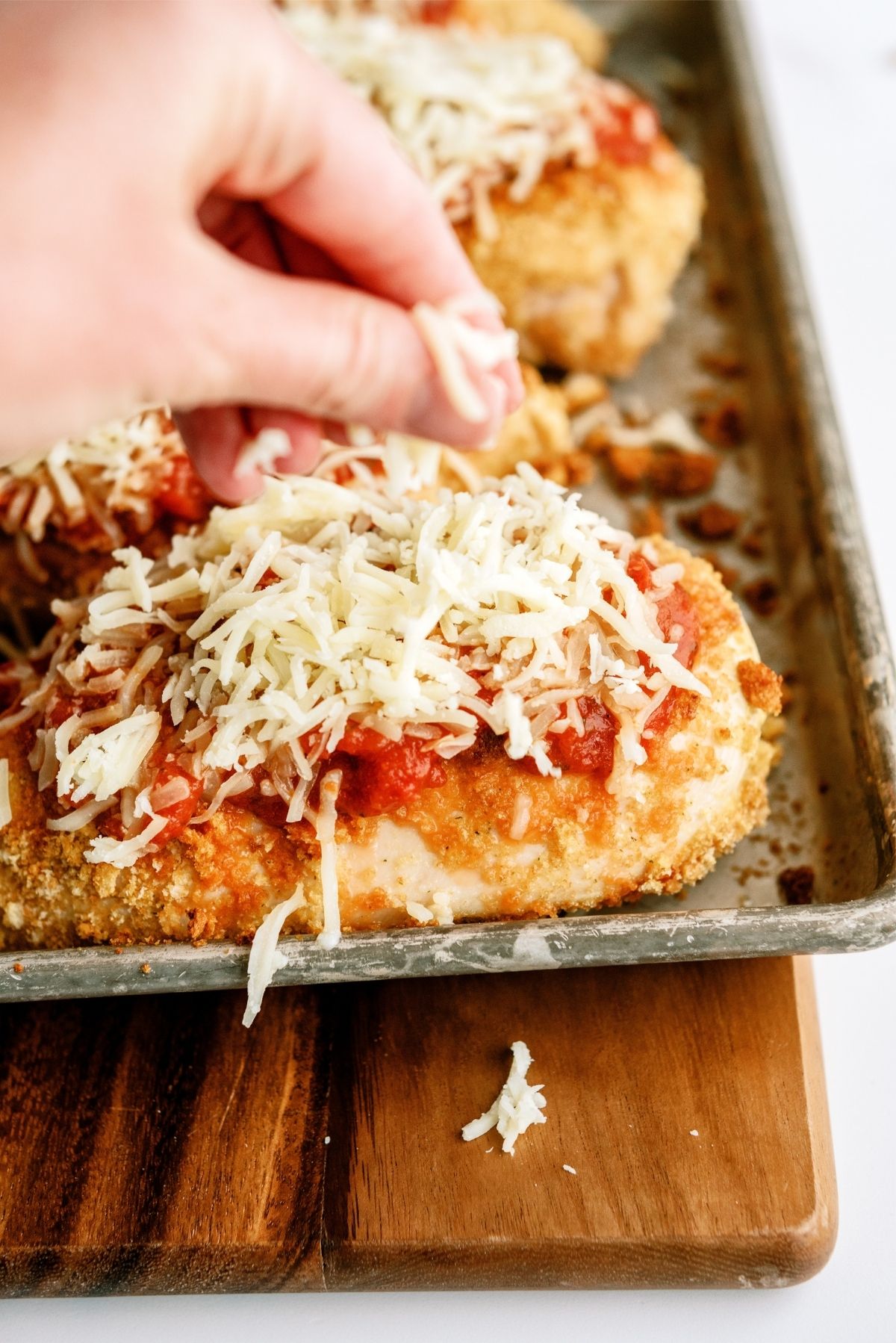 Putting cheese on top of Baked Crispy Chicken Parmesan