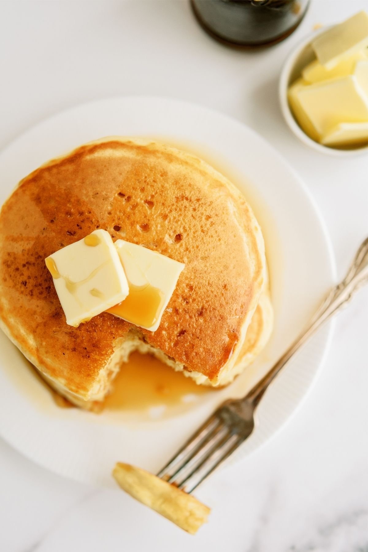 Stack of Cracker Barrel Buttermilk Pancakes with butter and syrup on top and a fork slicing a bite out of it.