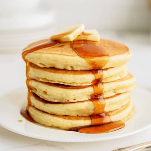 A stack of Cracker Barrel Buttermilk Pancakes on a white plate topped with butter and syrup.