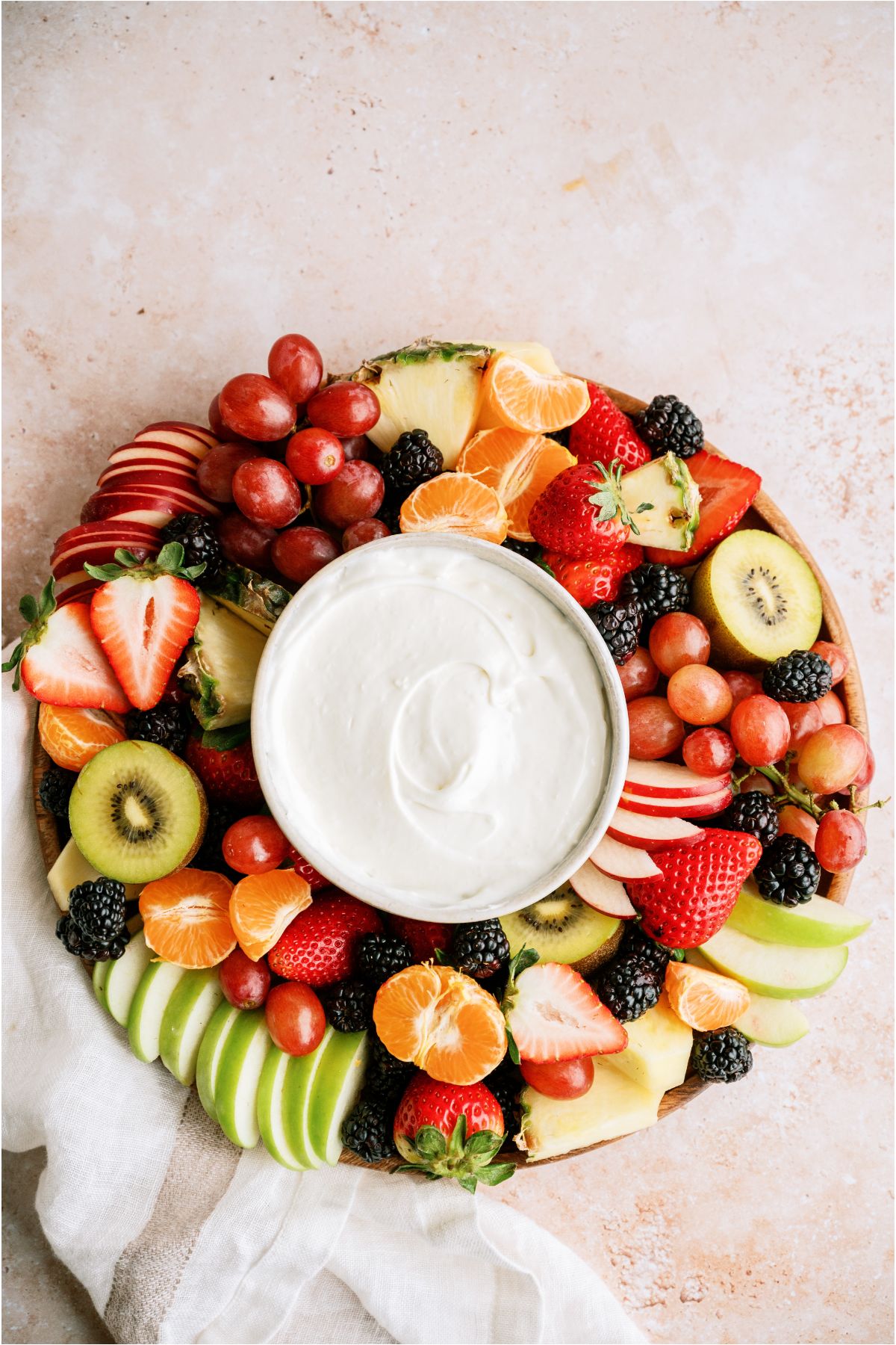 Top view of a platter of sliced fruit with a small bowl of Easy Cream Cheese Fruit Dip in the center.