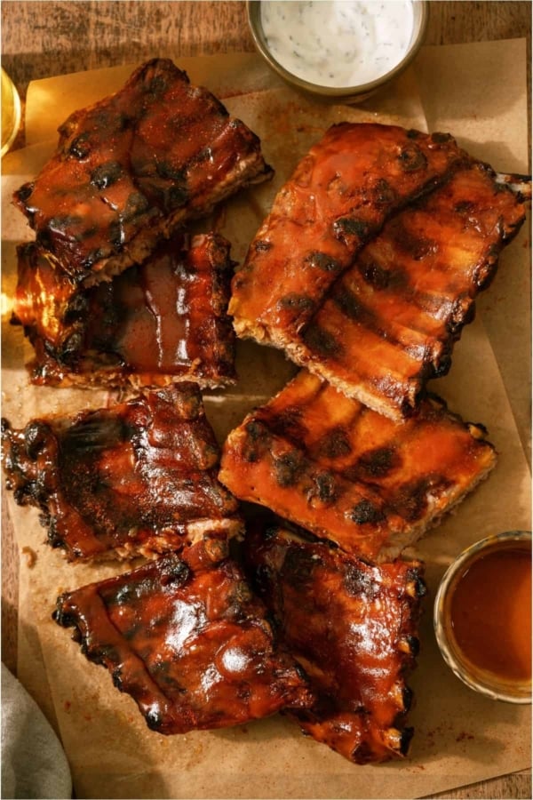 Easy Smoked Bbq ribs on a cutting board with sauce and dipping sauce.