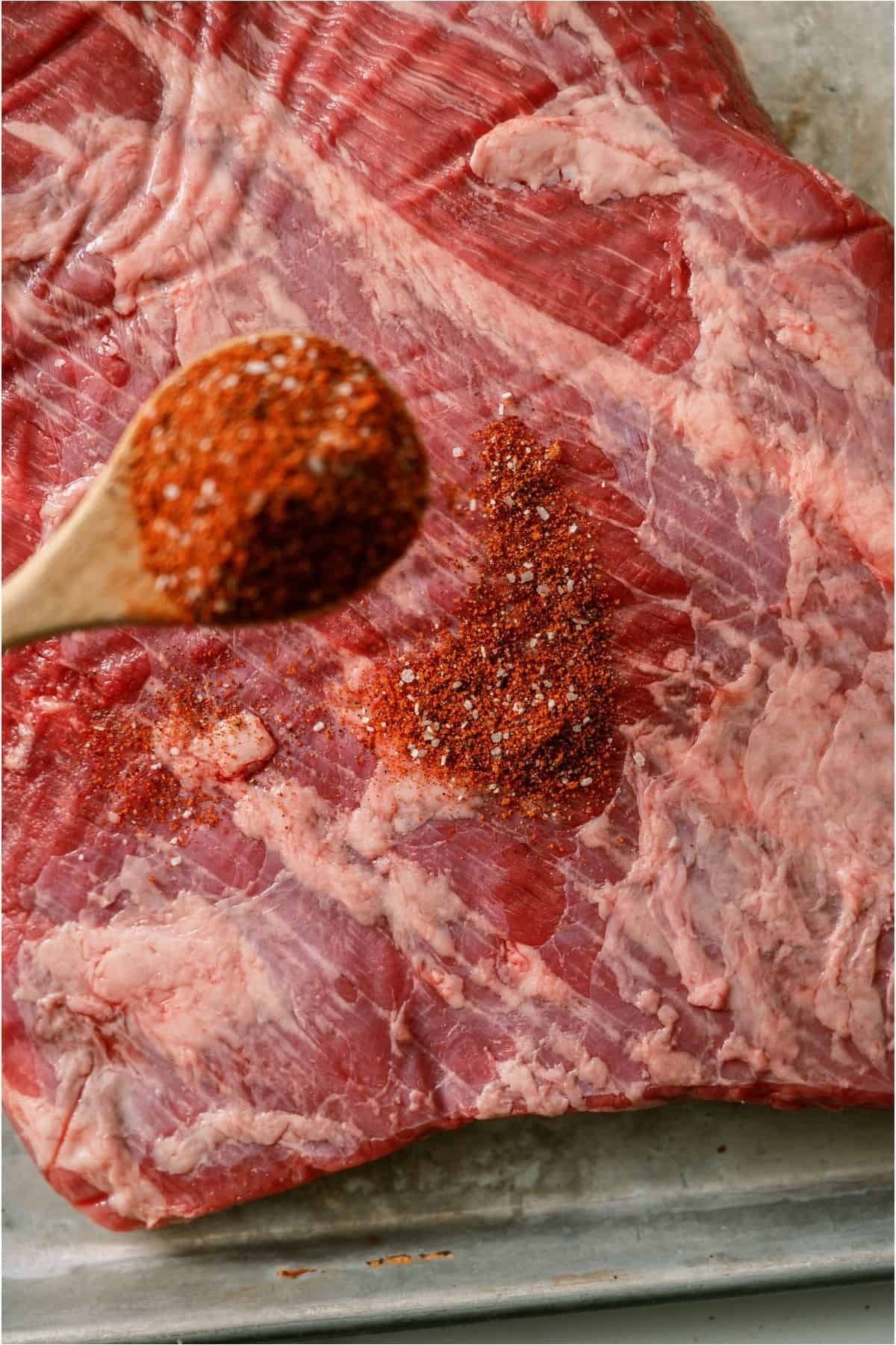 A spoon sprinkling rub on top of raw brisket.