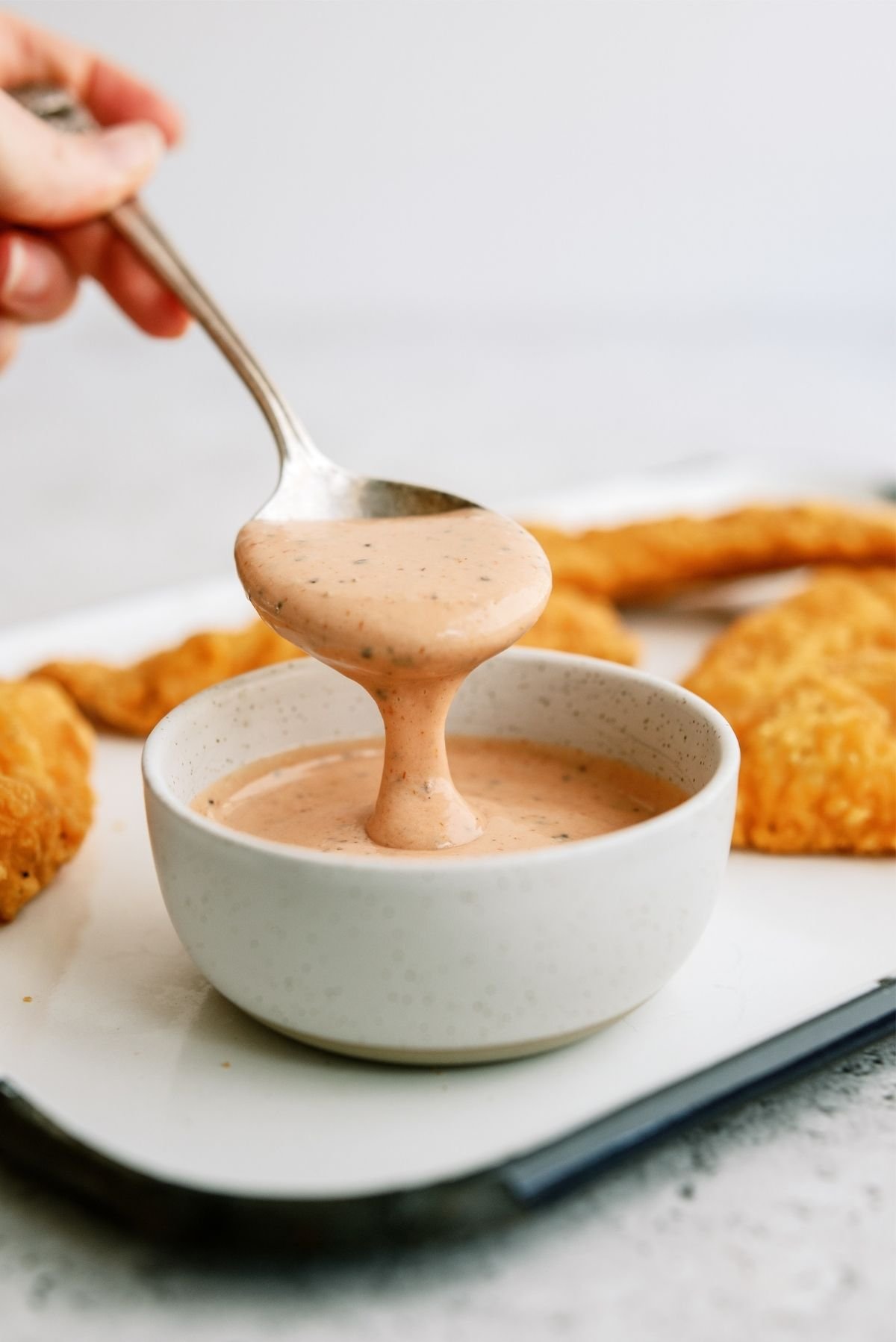 A spoonful of Raising Cane’s Chicken Sauce above a small bowl filled with sauce
